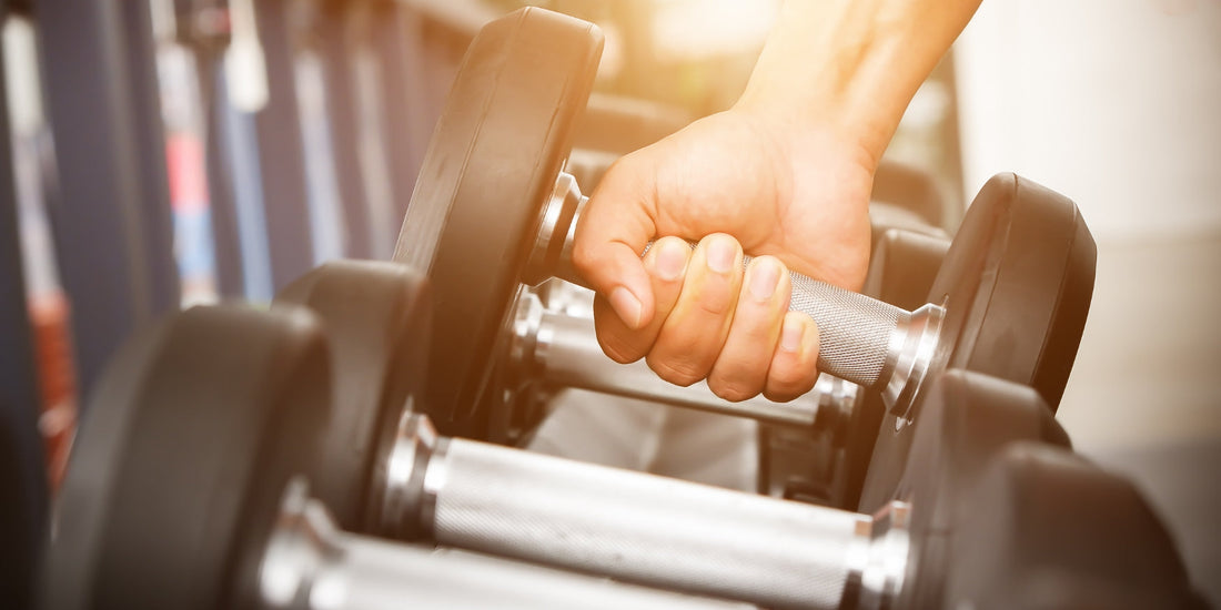 Dumbbells in een sportschool, waarbij een persoon een dumbbell oppakt voor een oefening.