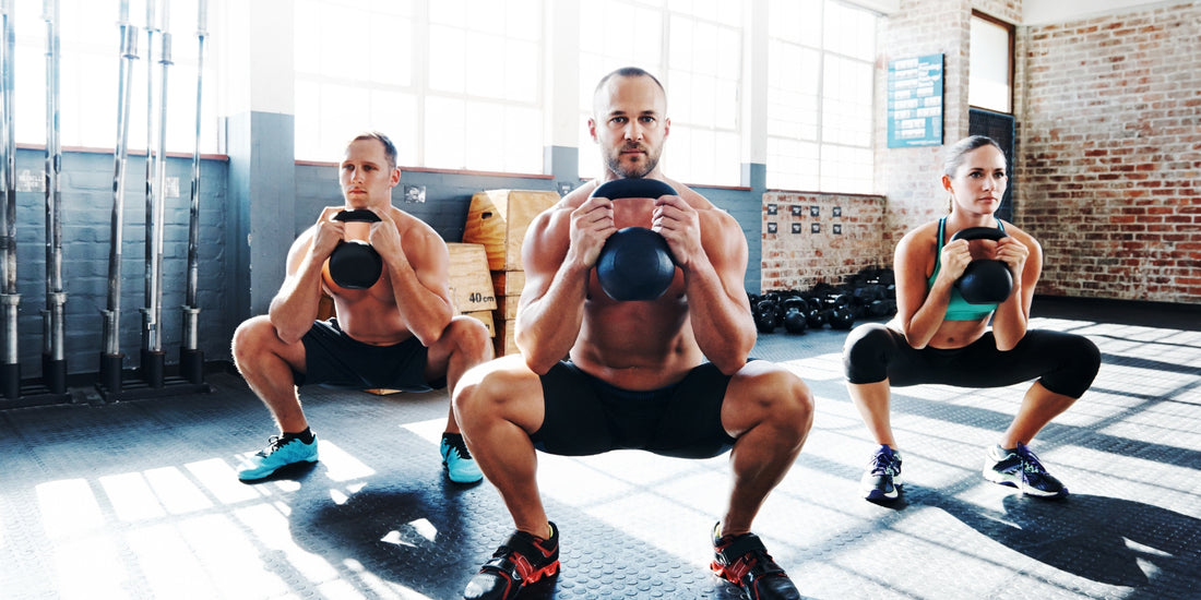 3 personen doen een full body workout oefening. Squats met kettlebell.