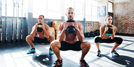 3 personen doen een full body workout oefening. Squats met kettlebell.