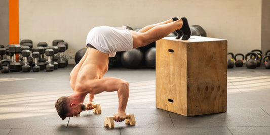 Een sporter traint zijn schouders en core met een box pike push-up in de gym. Deze oefening simuleert een overhead press en verbetert schouderkracht en stabiliteit.