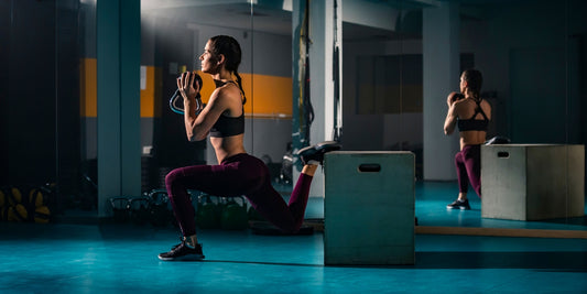 Jonge sportvrouw doet een split squat oefening in een lege gym met een kettlebell in haar handen.